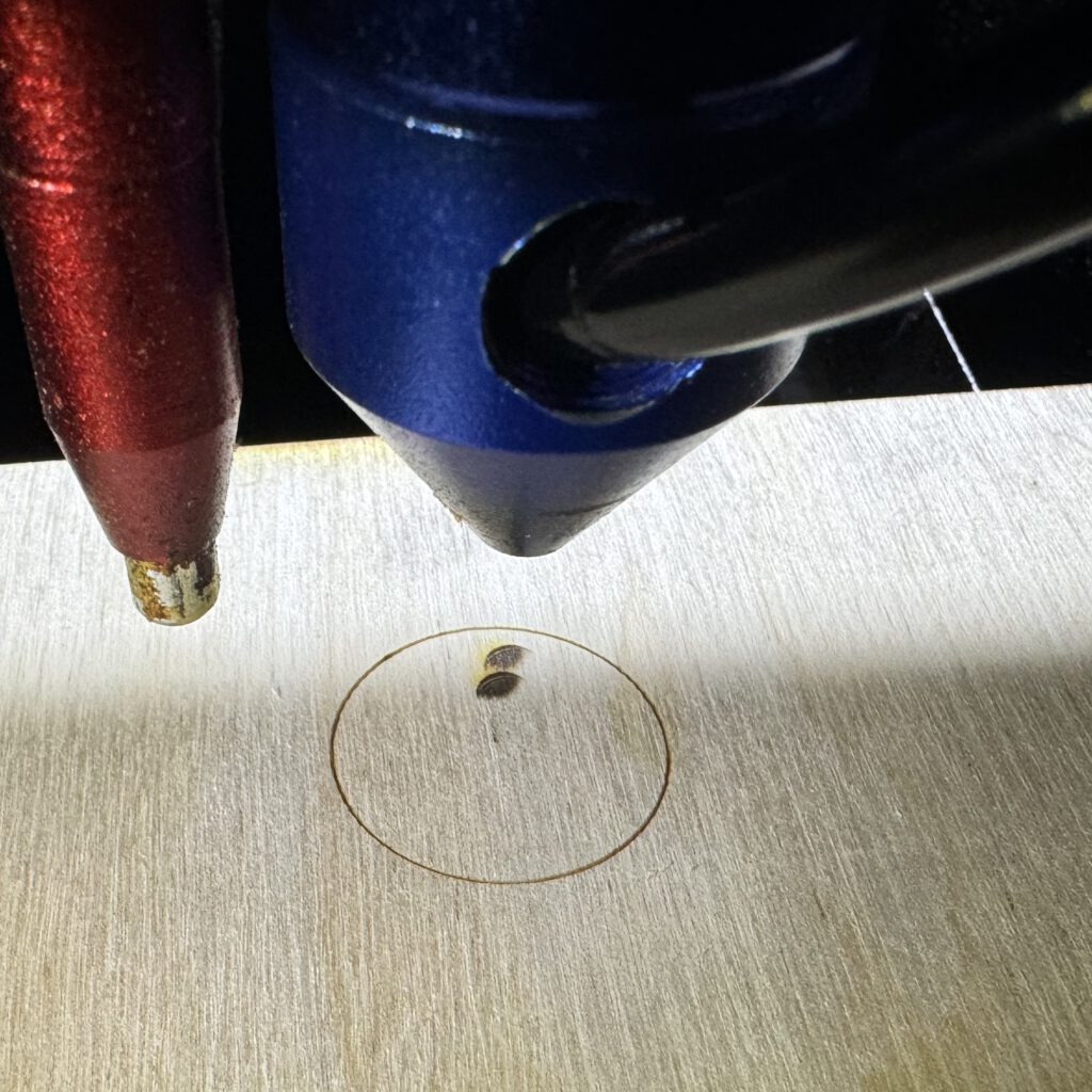 Nozzle above a workpiece with a marked circle and two laser impact points inside.
