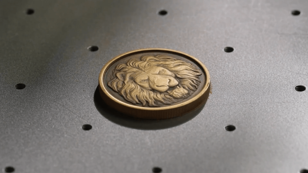 Metal coin with engraved lion head on the xTool F1 Ultra work surface.